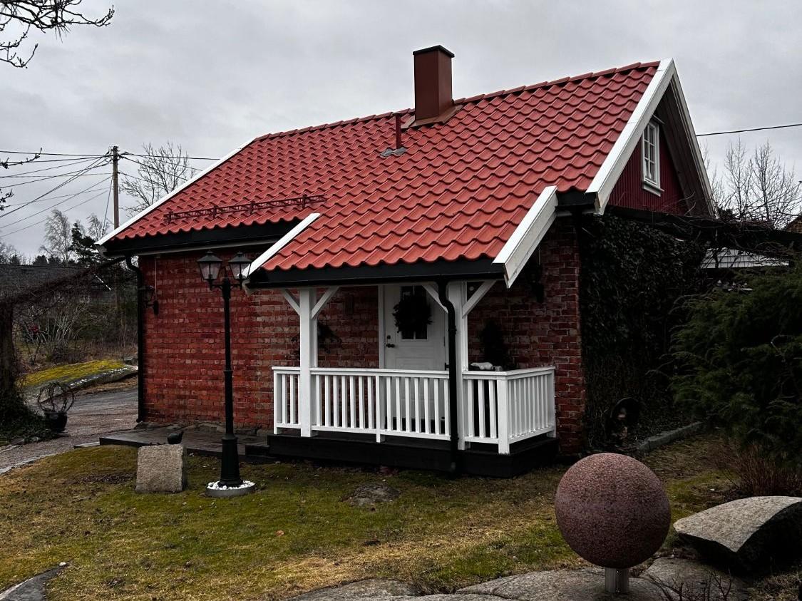 Rødt murhus med ny takstein og veranda med hvitt rekkverk